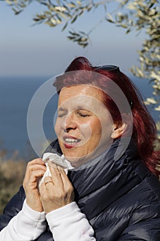 Woman sneezing, blowing nose into tissue above sea coast