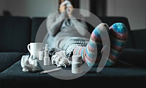 Woman sneezing and blowing nose with tissue and handkerchief. Sick and ill person with flu, cold medicine and woolen socks. photo