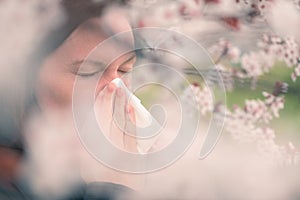 Woman sneezing in front of blooming cherry tree in spring