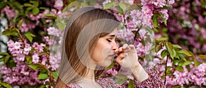 Woman sneezing into a handkerchief near a tree full of blossoms. She is suffering from seasonal spring allergy. Pollen