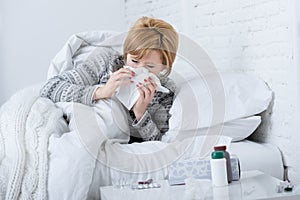 Woman with sneezing nose blowing in tissue on bed suffering cold flu virus symptoms having medicines tablets pills