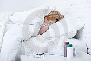 woman with sneezing nose blowing in tissue on bed suffering cold flu virus symptoms having medicines tablets pills