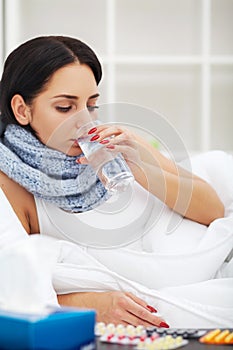 Woman with sneezing nose using tissue on bed suffering cold flu