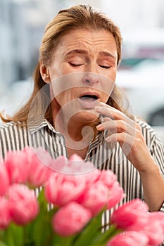 Woman sneezing after smelling flowers having allergy