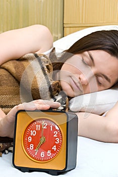Woman snoozing a red alarm clock photo