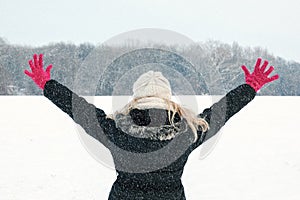 woman in snow showing her back and facing forest with hands raised