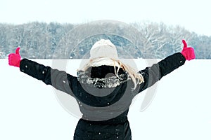 Woman in snow showing her back and facing forest with thumbs up