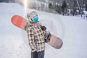 Woman snowboarder on a sunny winter day at a ski resort wearing a medical mask during COVID-19 coronavirus