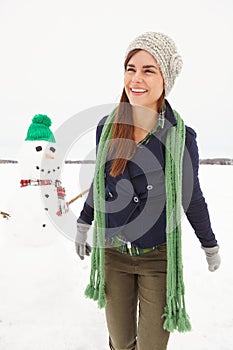 Woman, snowman and happy in nature on vacation with thinking, clothes and adventure in cold. Person, ice character and