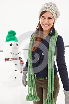 Woman, snowman and happy in portrait on vacation in nature with clothes for adventure in cold. Person, ice character and