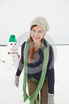 Woman, snowman and smile for portrait in winter with laugh, clothes or adventure on holiday. Person, snow sculpture and