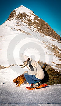 woman on snowshoes outdoors on snowy mountain trail petting her dog who is having fun digging