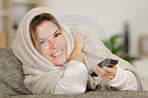 woman snuggled under blanket using remote control