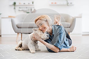 Woman snuggling cute pet& x27;s head on floor near sofa indoors