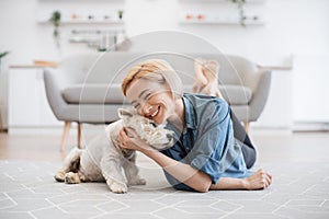 Woman snuggling cute pet& x27;s head on floor near sofa indoors