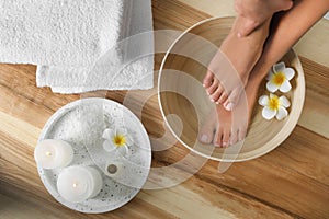 Woman soaking her feet in dish with water and flowers on wooden floor. Spa treatment