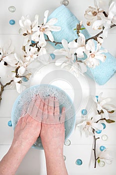 woman soaks her hands in a bowl with soapy water and sea pebbles for a delicate manicure spa procedure in the salon