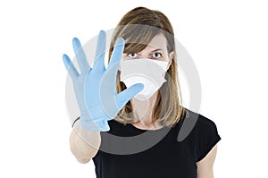 Woman social distancing from corona virus wearing a protective white face mask and medical gloves holding up hand saying stop.