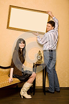 Woman on sofa and man hang up on wall picture