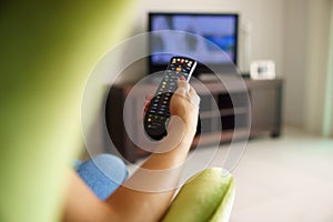 Woman on sofa watching tv changing channel with remote