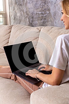 Woman on sofa working on laptop with mockup blank screen. Empty copy space on monitor for advertisement. Black screen.