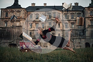 Woman sorceress reads book and flies in air against backdrop of ancient castle.