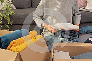 Woman sorting clothes and packing into cardboard box. Donations for charity, help low income families, declutter home