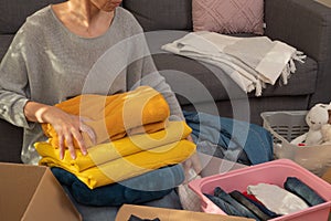 Woman sorting clothes and packing into cardboard box. Donations for charity, help low income families, declutter home