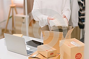 A woman sorting clothes and packing them into a cardboard box for selling online at her home . Business Owner concept