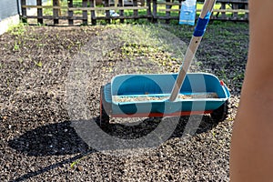 A woman sows grass with a wheel seed drill, visible grains of grass and black earth.