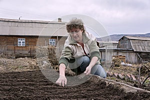 The woman sows the seeds in the ridge in the garden, against the background of the village.