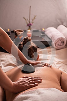 Woman in a spa receiving a relaxation massage with scented candles, incense, scent flowers, and obsidian stones with towels. 3.