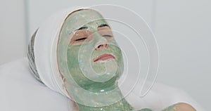 Woman in spa salon. Face mask. Beautiful girl lying on the couch with a green mask in the in cosmetology clinic