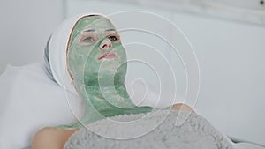 Woman in Spa Salon. Face Mask. Beautiful girl lying on the couch with a green mask in the in cosmetology clinic. Slow