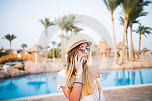 Woman speak on phone relaxing near swiming pool. Summer vocation.