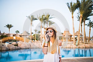 Woman speak on phone relaxing near swiming pool. Summer vocation.