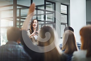 Woman speaker at seminar, audience with hands up for questions and answers at training presentation or meeting. Feedback