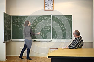 Woman speaks with pointer near blackboard with