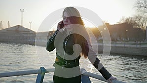 Woman speaks on smartphone, develops hair in backlight, mobile phone in hand of young woman, conversation on cell