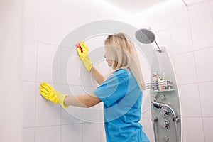 Woman with special cleaning sponge cleaning wall tiled surface in bathroom.