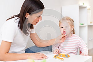 Woman speech therapist helps cute girl to learn correct pronunciation and literate speech