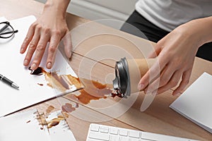 Woman spilled coffee on wooden office desk, closeup