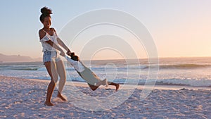 Woman spinning in a circle her daughter at beach