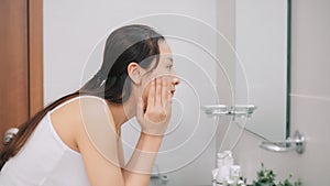 Woman splashing face with water above bathroom sink