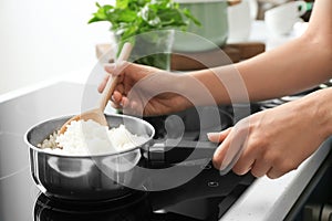 Woman with spoon stirring rice in saucepan, closeup