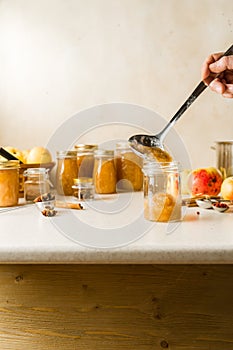 Woman spooning fresh homemade applesauce in glass jars on kitchen table