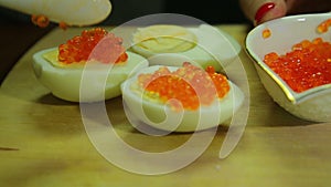 A woman spooning red caviar on a half of a boiled egg