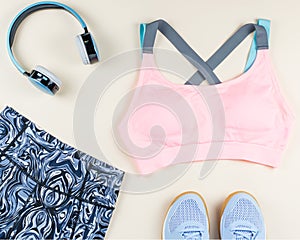 Woman sport bra, leggins, sneakers, headphones and fitness tracker on neutral background. Sport fashion concept.