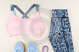 Woman sport bra, leggins, sneakers, headphones and fitness tracker on neutral background. Sport fashion concept.