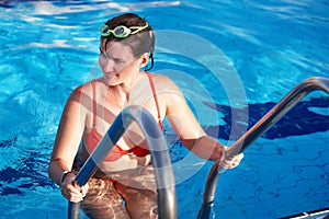 Woman in sport goggles leaves swimming pool.